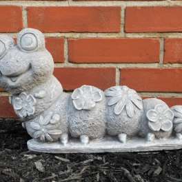 Stone caterpillar garden statue with flower decorations against a brick wall