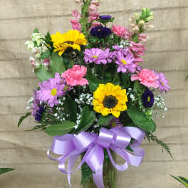Mixed bouquet with sunflowers, purple daisies, and pink carnations in a glass vase