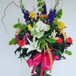 Tall mixed flower arrangement in a glass vase with a pink ribbon