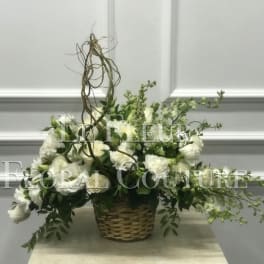 White floral arrangement in a woven basket with trailing greenery