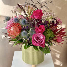 Bouquet of pink roses and spiky flowers in a ribbed green vase