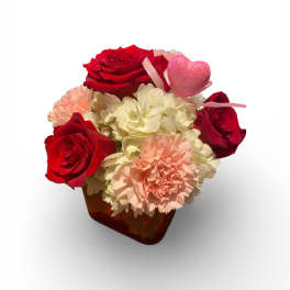 Red roses and pale carnations in a small vase with a pink heart pick