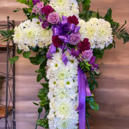 Cross-shaped floral spray with white chrysanthemums, purple roses, and a purple ribbon