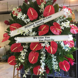 Standing sympathy spray with red tropical flowers, white orchids, and message ribbons on an easel