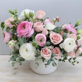 Low pastel arrangement of pink roses and ranunculus in a white ceramic bowl-style vase