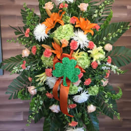 Large floral standing spray with orange lilies and a green shamrock accent