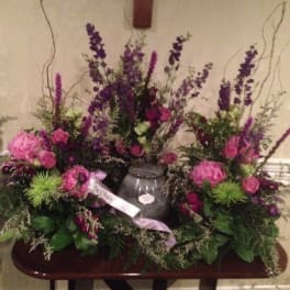 Large purple and pink floral funeral arrangement with a vase centerpiece