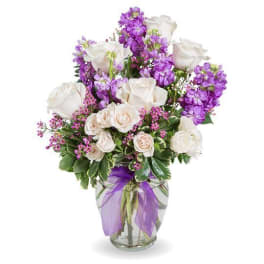 White roses and purple flowers in a glass vase with a purple ribbon