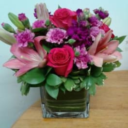 Pink and purple flower arrangement in a square glass vase