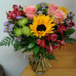 Bouquet of pink roses, a sunflower, and mixed blooms in a glass vase
