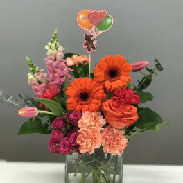 Bright mixed bouquet in a square glass vase with a balloon topper