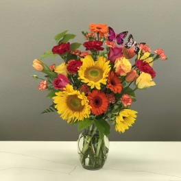 Bright mixed bouquet with sunflowers, roses, gerbera daisies, and carnations in a glass vase