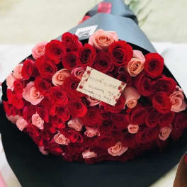 Large bouquet of red and pink roses wrapped in black paper with a small card attached