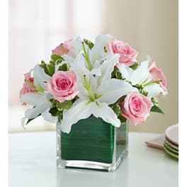 Pink roses and white lilies arranged in a clear square vase