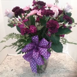 Purple and pink mixed flower bouquet in a glass vase with a polka-dot ribbon