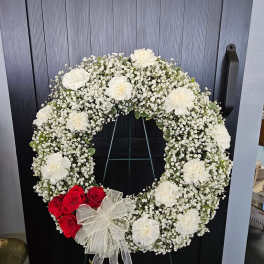 White floral wreath with red roses and a sheer bow on a stand
