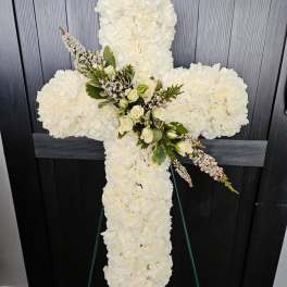 White floral cross on an easel with small roses and greenery at the center