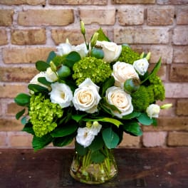 White roses and green blooms arranged in a glass vase