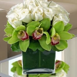 White roses and green orchids arranged in a glass vase