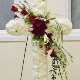 White floral cross with red roses and lilies on an easel