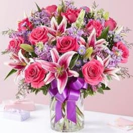 Pink roses and lilies in a glass vase with a purple ribbon