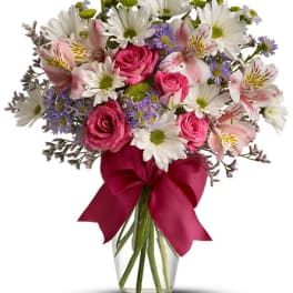 Bouquet of pink roses, white daisies, and alstroemeria in a glass vase with a burgundy ribbon