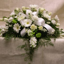 White floral casket spray with ribbon on a beige cloth backdrop