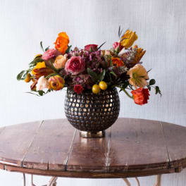 Mixed bouquet of orange, pink, and red flowers in a dark textured vase