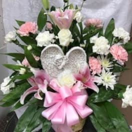Pink and white floral arrangement with a pink ribbon and angel wings