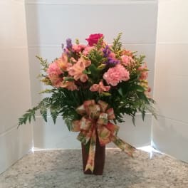 Pink and peach mixed flower arrangement in a tall vase with a ribbon