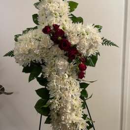 White floral cross arrangement with red roses on a stand