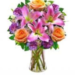Bouquet of pink lilies, orange roses, and purple flowers in a glass vase