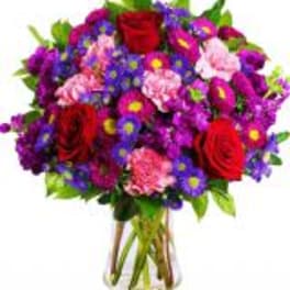 Bouquet of red roses, purple flowers, and pink carnations in a glass vase