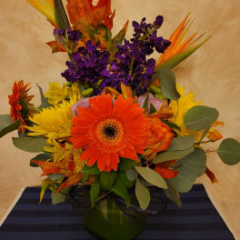 Bright mixed bouquet with orange gerbera daisies and purple flowers in a green vase