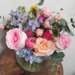 Bouquet of pink and peach roses with blue hydrangeas in a glass vase