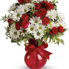 Red roses and white daisies in a red vase with a ribbon