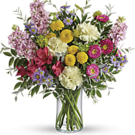 Mixed bouquet of pink, yellow, white, and purple flowers in a glass vase
