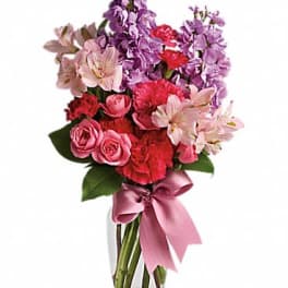Pink and purple bouquet in a clear glass vase with a satin ribbon
