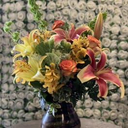 Bouquet of lilies, roses, and orchids in a dark glass vase