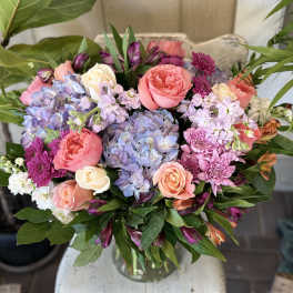 Bouquet of pink roses, blue hydrangea, and purple flowers in a glass vase