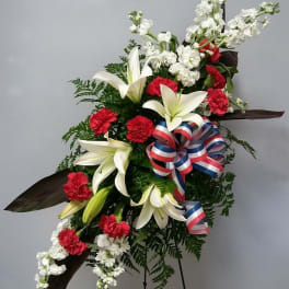 Standing floral spray with white lilies, red carnations, and a patriotic ribbon