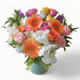 Colorful bouquet of peach gerbera daisies, roses, and white orchids in a round vase