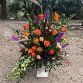 Tropical floral arrangement with orange roses and bird of paradise in a white pedestal vase