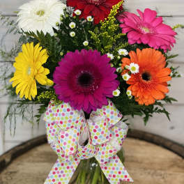 Colorful gerbera daisy bouquet in a glass vase with a polka-dot bow