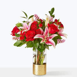 Red roses and pink lilies arranged in a glass vase with a gold base.
