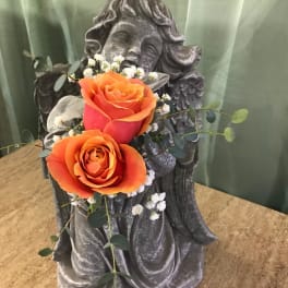 Two orange roses arranged on a stone angel statue