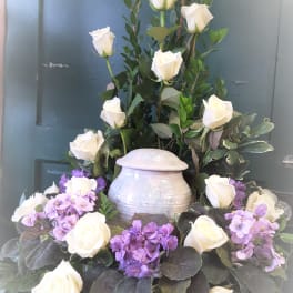 White roses and purple flowers arranged in a tall urn centerpiece