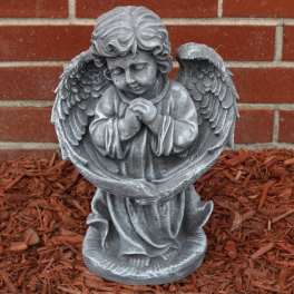 Gray angel statue with folded hands in front of a brick wall