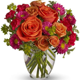 Orange roses and magenta daisies in a clear glass vase