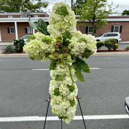 Large floral cross on an easel with pale green and white blooms